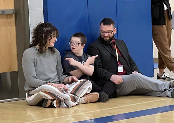 student sitting on floor with principal and teacher in gym