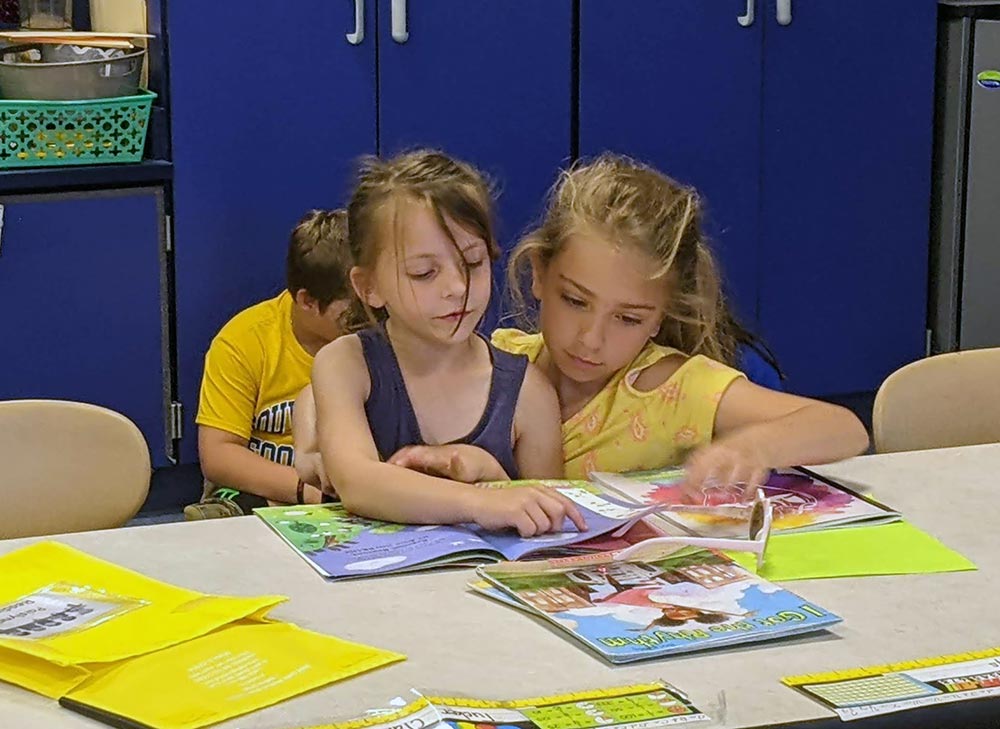 2 elementary girls sitting together at a desk reading