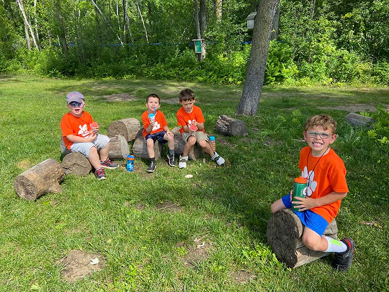 elementary students in matching orange t-shirts sitting on logs