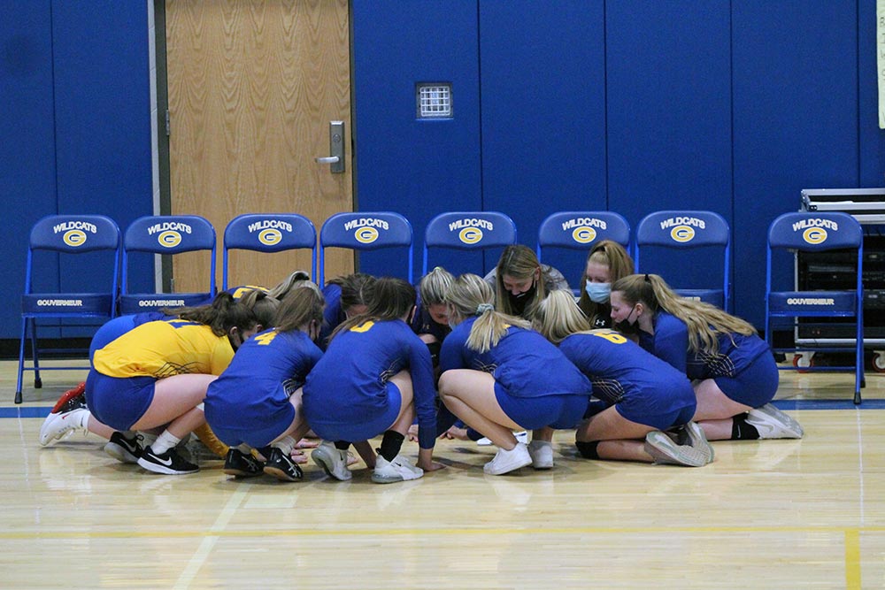 Girls volleyball team kneeling in a huddle 