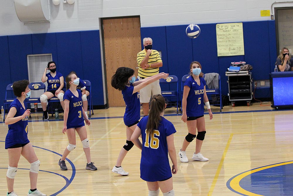 JV volleyball players underhanding the ball over the net