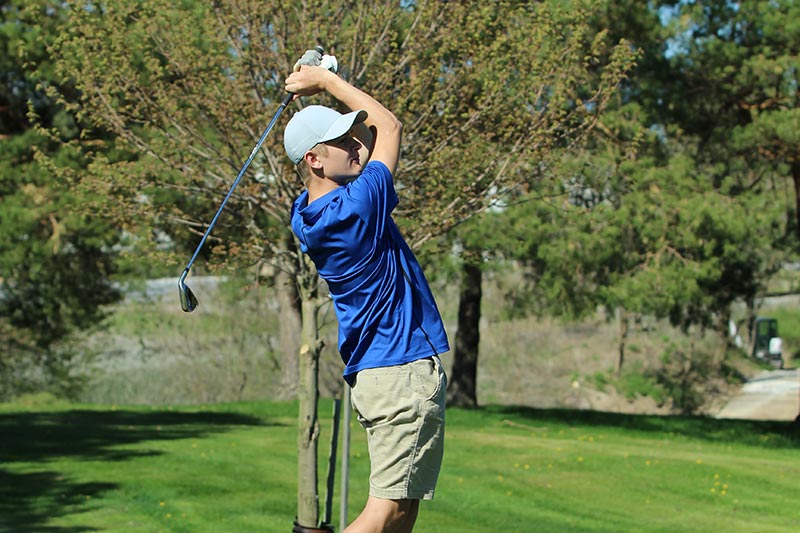 varsity golfer at the top of his swing from the tee