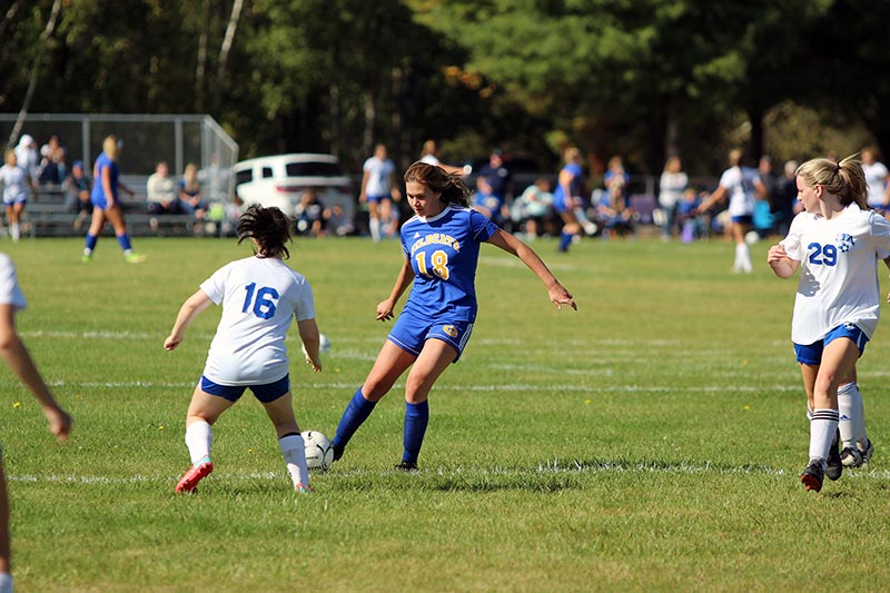JV girls soccer player striking the ball towards the net