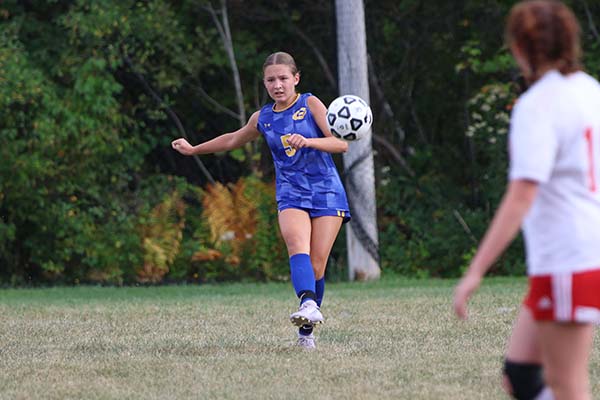 JV girls soccer player striking the ball towards the net