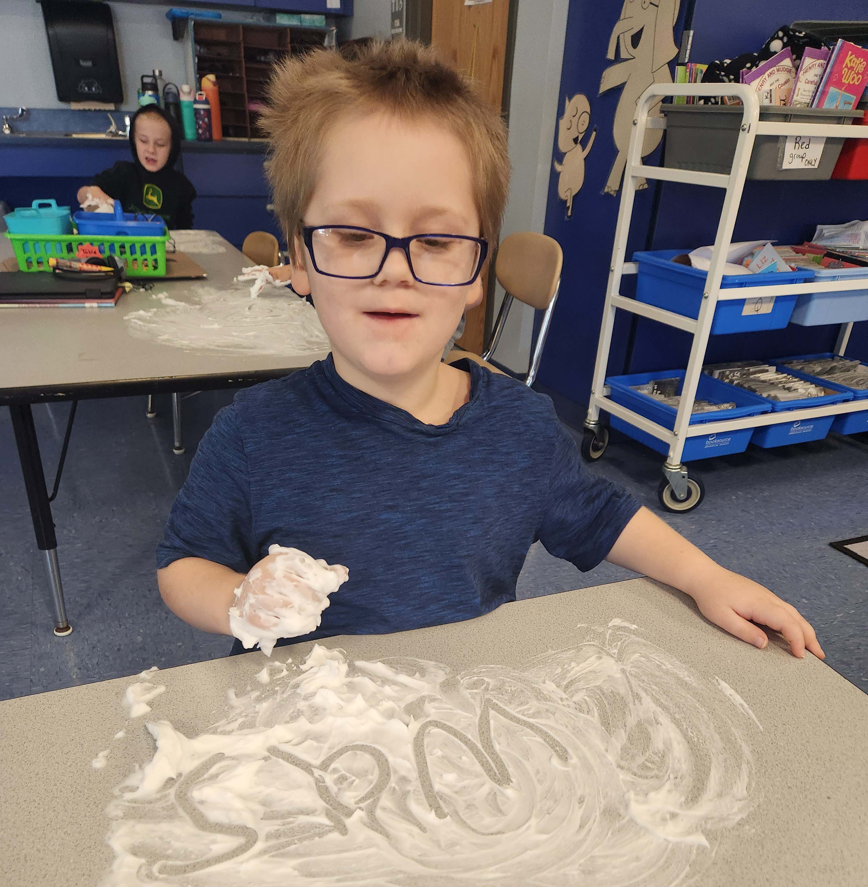 young male student spelling on desk with shaving cream on it